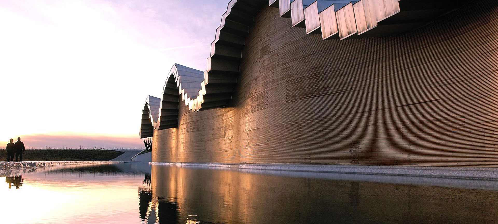 Modern gebouw weerspiegelt in water bij zonsondergang.