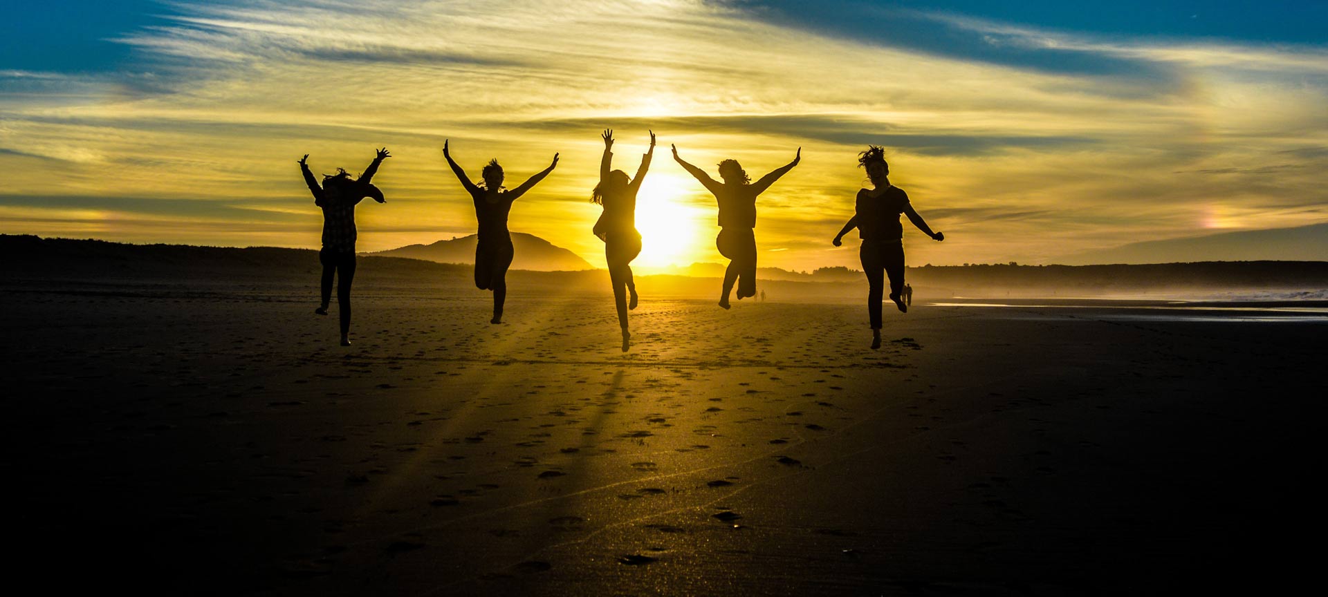 Vrienden springen op strand bij zonsondergang.