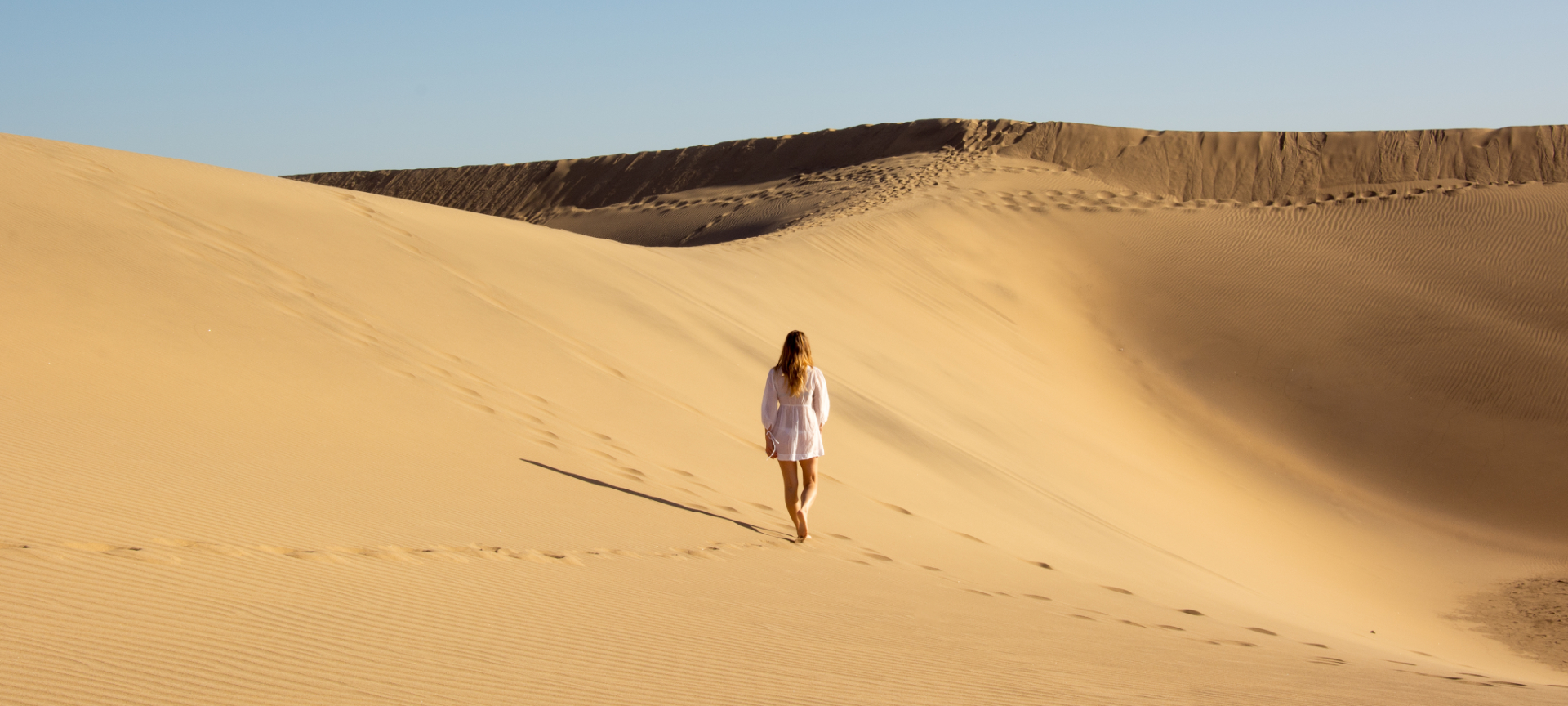 Persoon wandelt in uitgestrekte zandduinen.