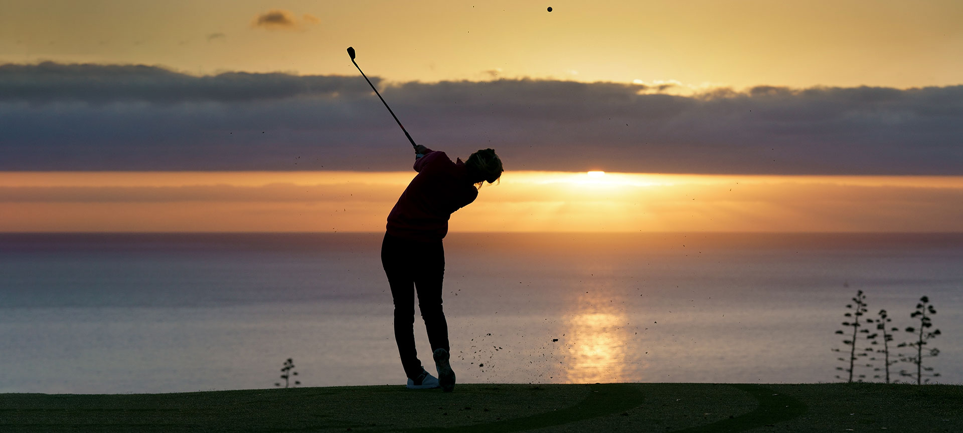 Golfer slaat bal bij zonsondergang aan zee.